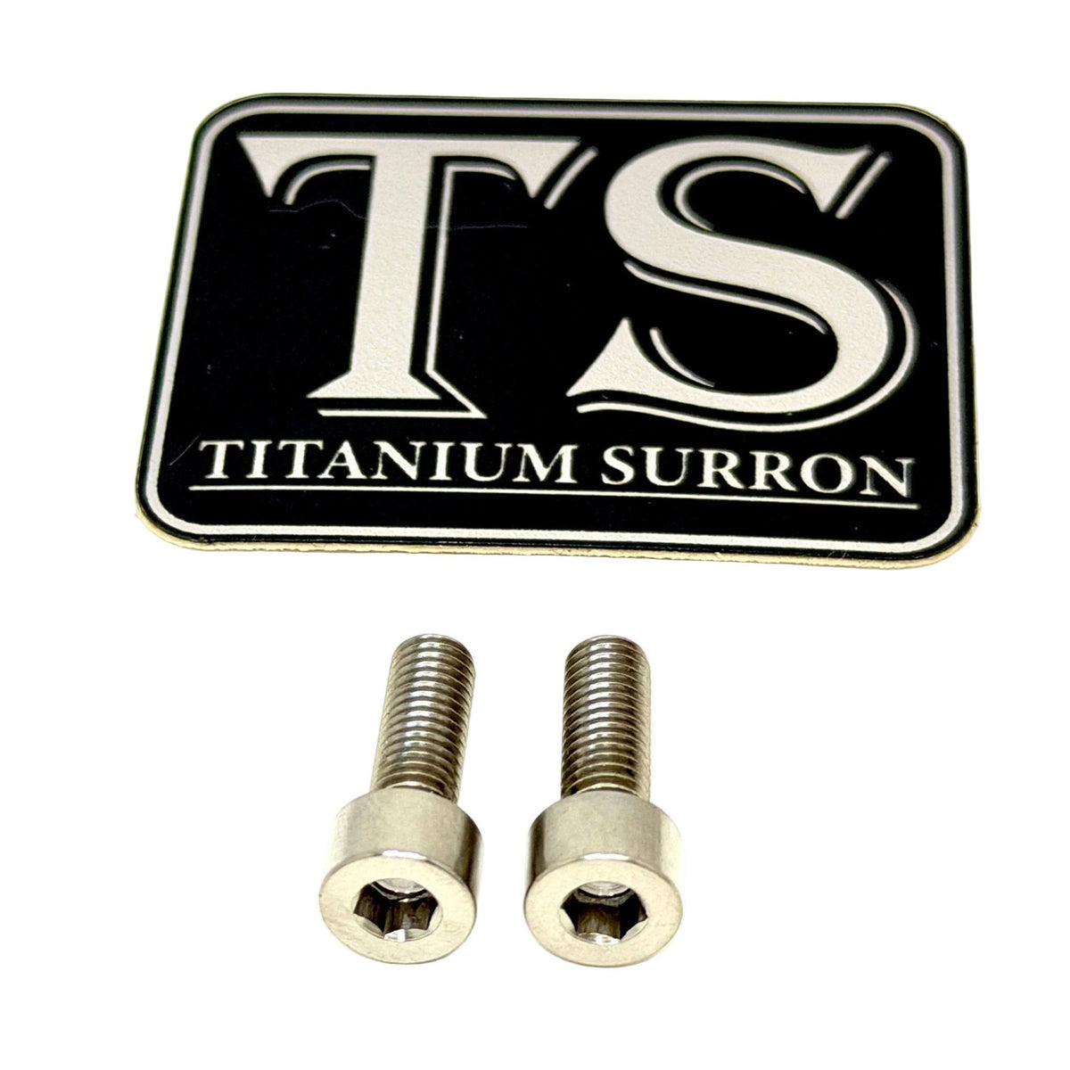 A black rectangular badge with silver 'TS' lettering and 'TITANIUM SURRON' text, shown above two silver metal screws on a white background.