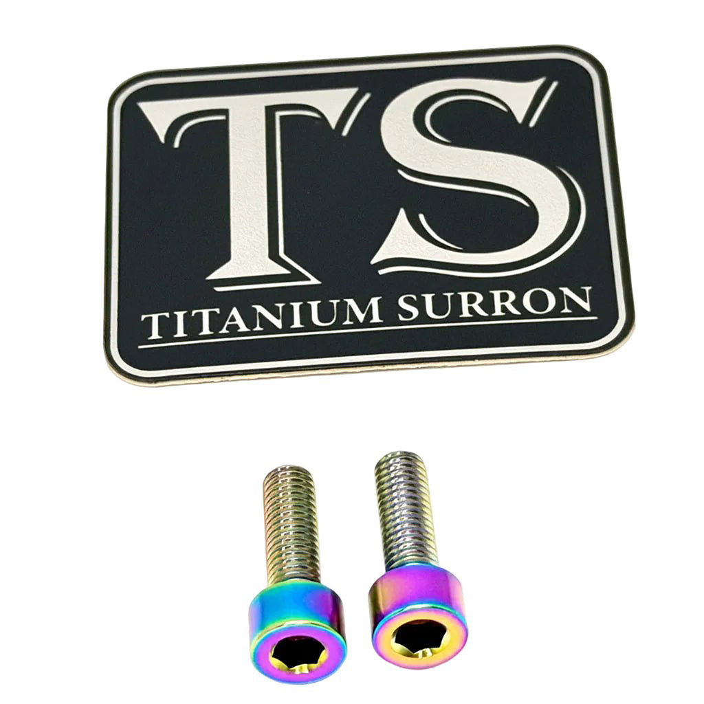 A black rectangular badge or emblem with silver lettering reading 'TS' and 'TITANIUM SURRON' below it, shown above two small metallic hex screws with iridescent rainbow-colored heads on a white background.