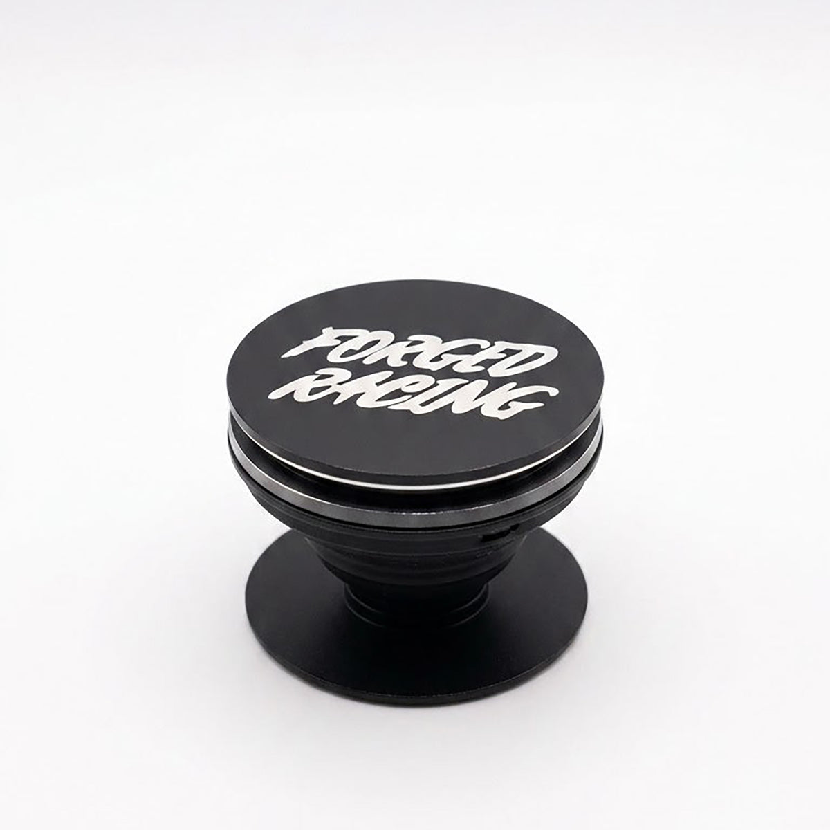 A black pop-up phone grip with 'FORGED RACING' printed in white stylized lettering on the top cap, set against a plain white background.