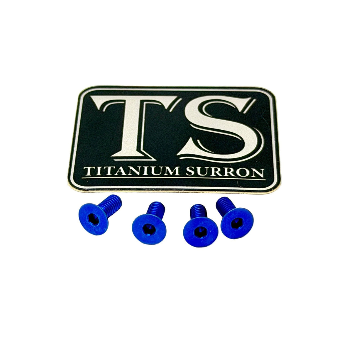 A black rectangular badge or emblem with silver 'TS' lettering and 'TITANIUM SURRON' text, shown above four small blue screws on a plain white background.