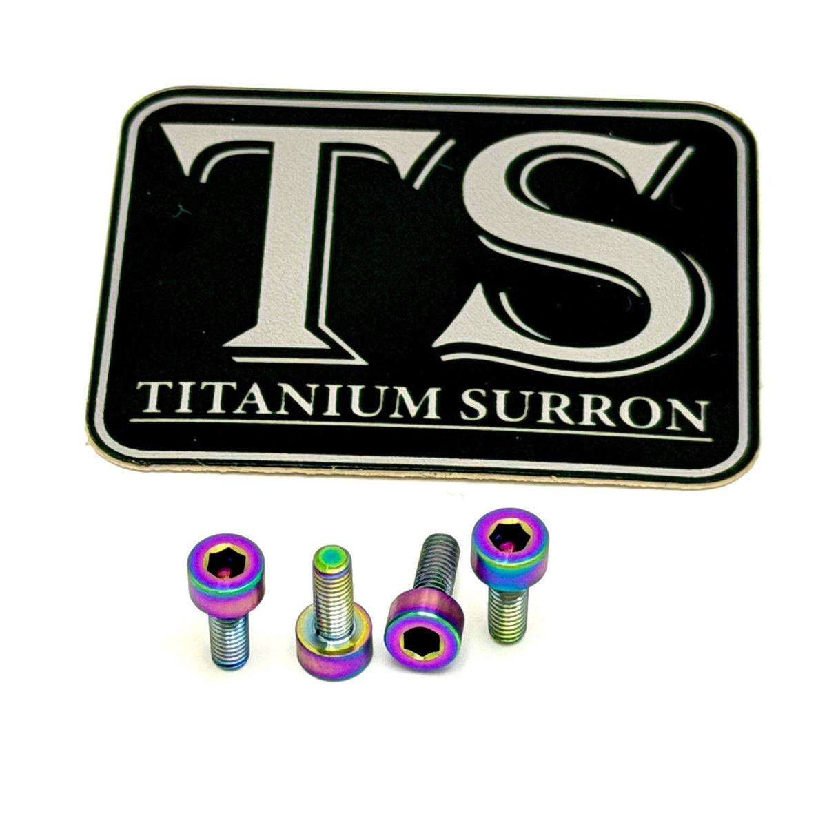 A set of four titanium motorcycle or bicycle hardware bolts with a vibrant iridescent rainbow finish, displayed below a black and silver 'TS TITANIUM SURRON' logo plaque on a clean white background.