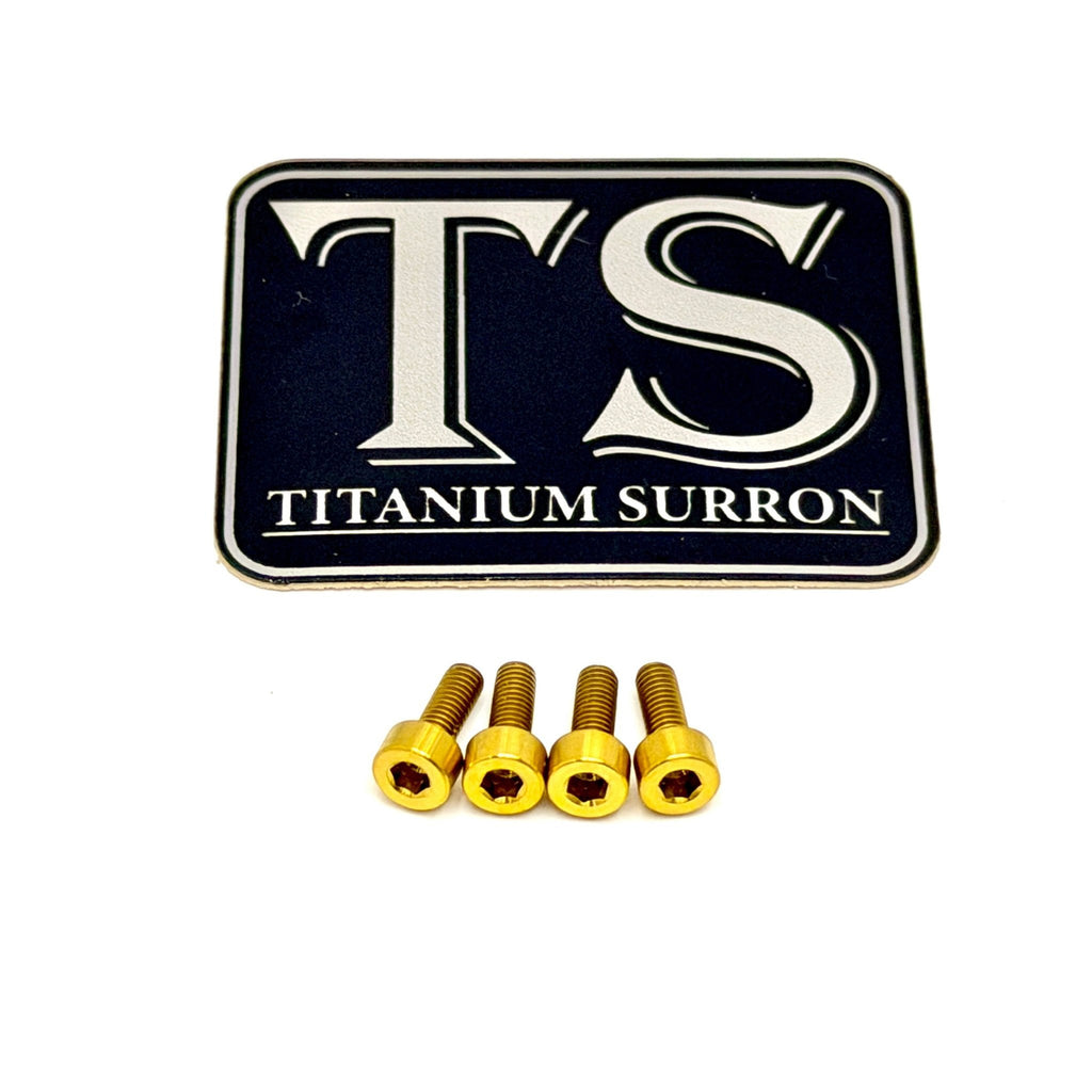 A black rectangular badge or emblem with rounded corners featuring large white 'TS' lettering and the words 'TITANIUM SURRON' below, shown above four small gold-colored hex screws on a plain white background.